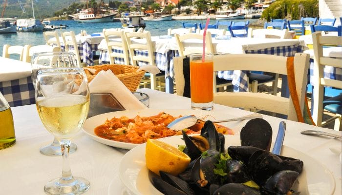 A waterfront Greek restaurant with a plate of mussels and a glass of wine, overlooking the sea.