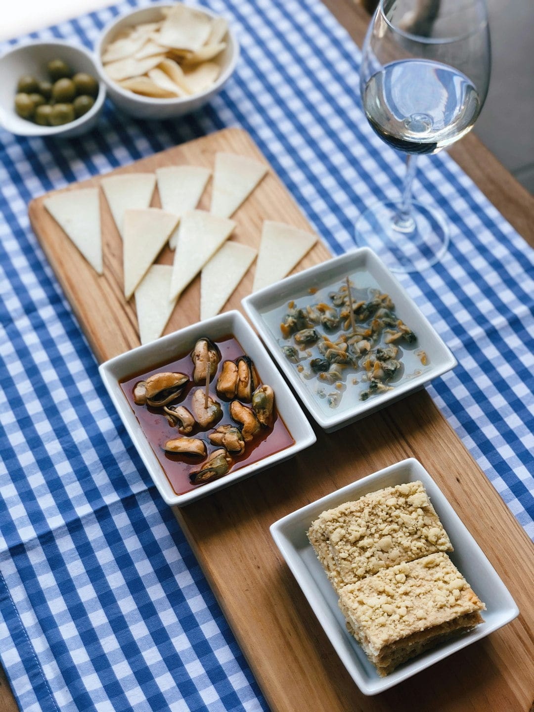 Table with blue checkered tablecloth, Spanish tapas, and a glass of wine, illustrating mealtime customs